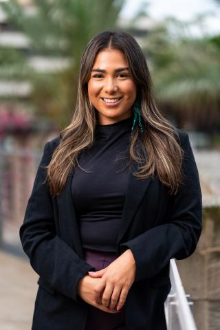 Picture of a cis-gendered female presenting person with long brown hair with black shirt and black jacket. 
