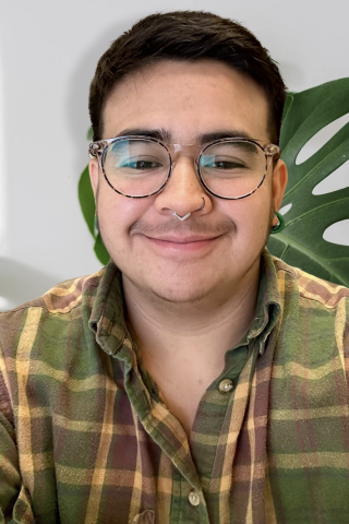 Portrait of person with glasses, a flannel and monastera leaves behind them