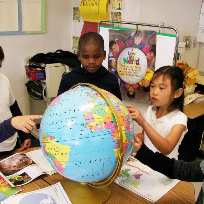Three grade school kids of diverse ethnicities point to a globe in a classroom